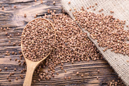 raw buckwheat in a wooden spoon on a dark brown wooden backgroundの写真素材