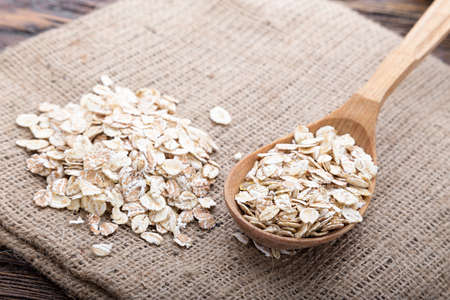 raw oat flakes in a spoon on a napkin from a sacking on a wooden tableの写真素材