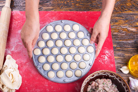Prepare raw homemade food - dumpling in metal strainer pelmennica. They have a traditional form. Pork, chicken mincemeat. Background is red.の写真素材
