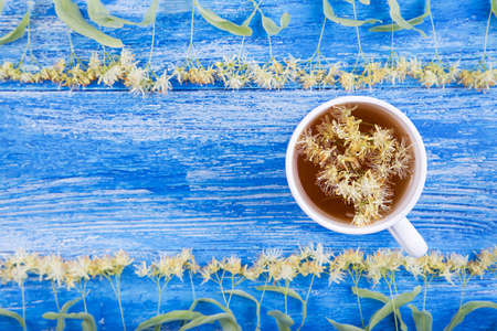 Linden tea in a cup on a wooden background. Around scattered fragrant linden flowersの写真素材