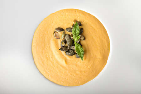 pumpkin cream soup in a white plate on a dark wooden table. on a soup are beans pumpkin and basil leaves. top viewの写真素材
