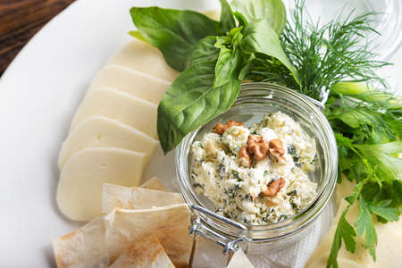 Cheese plate on a dark wooden table. Many kinds of cheese with basil, parsley, dill and pita on a plate. Horisontalの写真素材