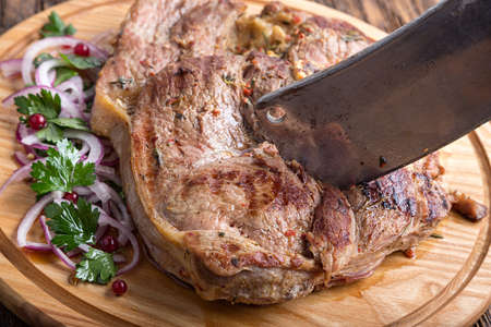 Medium rare grilled Beef steak Ribeye with onion on cutting board on dark wooden background. carving knife is in steak.の写真素材