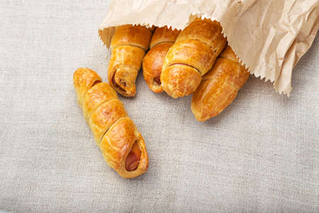 Sausage in the dough in a paper bag on a linen napkin, fast food, close upの写真素材