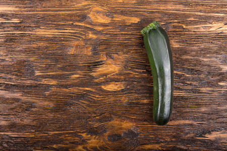 a fresh zucchini on a natural brown wooden background. Zucchini is vertical.の写真素材