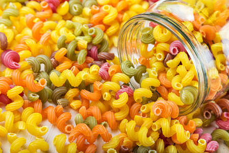 colored pasta in a jar and some scattered on the white wooden table