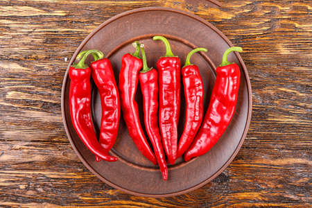 red pepper in a clay plate on dark wooden surface, top view