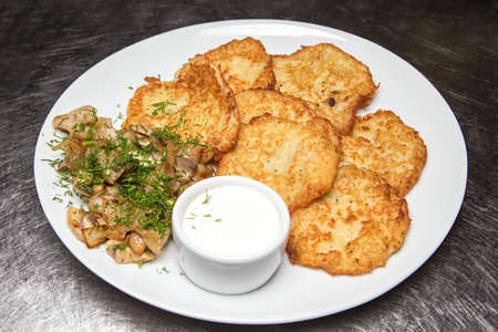 potato pancakes with sour cream and fried mushrooms with onion on a plateの写真素材