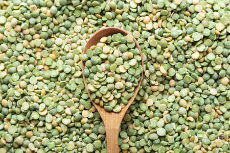 uncooked dry peas is scattered as a background, in the center there is a wooden spoonの写真素材