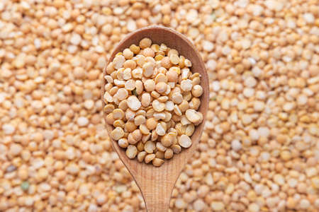uncooked yellow peas in a wooden spoon on a background of spillage of dry peasの写真素材