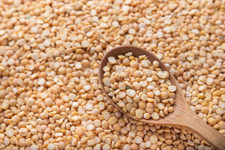 uncooked yellow peas in a wooden spoon on a background of spillage of dry peasの写真素材