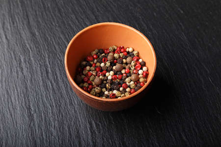multicolored peppers peas in a clay cup on a slate board,Horizontal photo with free space area for text or design.の写真素材