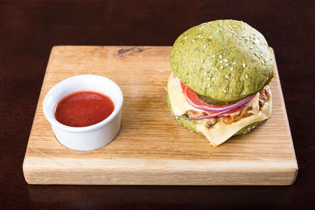 blue burger cutlet, vegetables and cheese, with sauce on a wooden boardの写真素材
