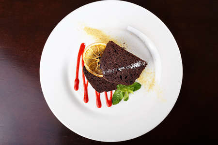 piece of chocolate cake on a plate, decorated with berry topping, mint and slice of lemonの写真素材