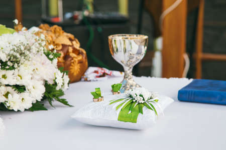 Traditional wedding loaf on the table, next to a bouquet of flowers, a pillow with rings and a wedding bowl.  Horizontal photoの写真素材