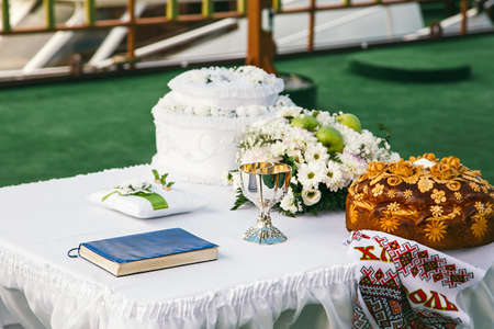 Traditional wedding loaf on the table, next to a bouquet of flowers, a pillow with rings and a wedding bowl.  Horizontal photoの写真素材