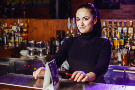 A barman girl at a bar, ready to take an order. Horizontal photoの写真素材
