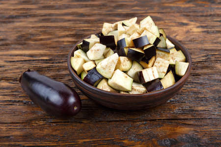 Diced eggplants in a clay plate on a wooden background, next to it is a whole eggplant. Horizontal photoの写真素材