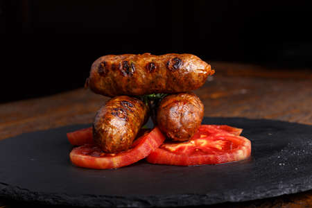 grilled sausages with tomato slices on a slate board on wooden backgroundの写真素材