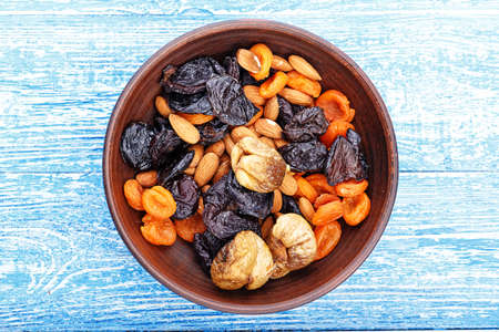 Dried figs, dried apricots and prunes in a mix with almonds in a clay plate on a wooden table, horizontal photoの写真素材