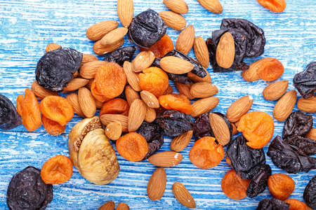 Dried fruits figs, dried apricots and prunes in a mix with almonds scattered on a wooden table, horizontal photoの写真素材