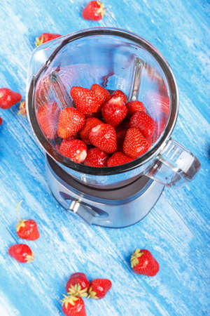 Fresh strawberries in blender on a wooden table. Next to the blender strewn strawberries.の写真素材