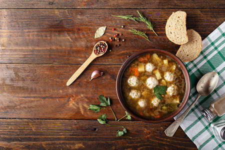 Soup with meatballs in a clay plate. Next to the plate is a napkin, bread and spices, space for textの写真素材