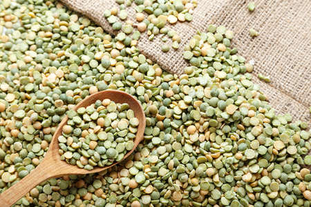 Dry green peas in a wooden spoon, peas scattered on a table, on a napkin with a natural texture,...