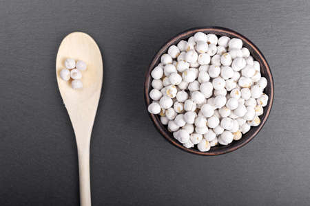 chickpeas in a bowl on black slate background; top view, lies next to wooden spoonの写真素材