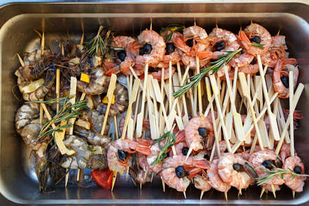 A lot of seafood on skewers, grilled shrimp in a metal container. Preparation for a banquetの写真素材