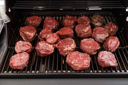A lot of raw cut medallions of veal on the grill. Outdoor barbecue