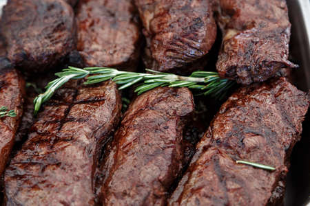 A lot of cooked veal steaks. On the steaks lies a branch of fresh rosemaryの写真素材