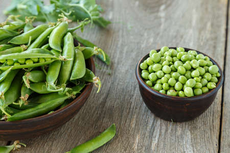 young peas in a clay plate on a wooden table. next to a plate are a pea pods.の写真素材