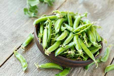 Green peas in a clay plate on a wooden table. It lies next to pea pods.