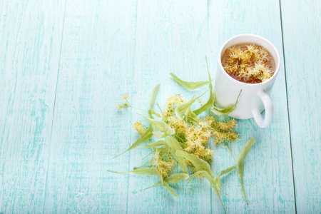 a cup of tea from a lime-tree, linden blossoms are scattered on the wooden tableの写真素材