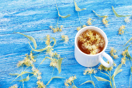 a cup of tea from a lime-tree, linden blossoms are scattered on the wooden tableの写真素材