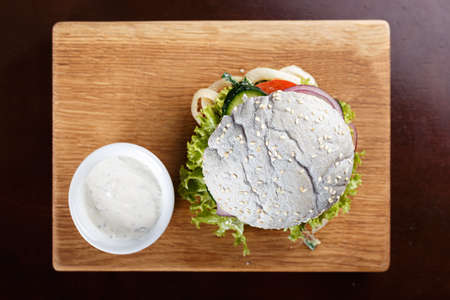 blue burger with fried squid and creamy spinach sauce on a wooden boardの写真素材