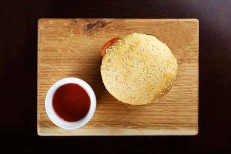 burger sprinkled with sesame seeds, served with sauce on a wooden board on a black backgroundの写真素材