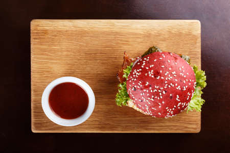 Red burger with cutlet, bacon and vegetables, sprinkled with sesame seeds on a blackboardの写真素材