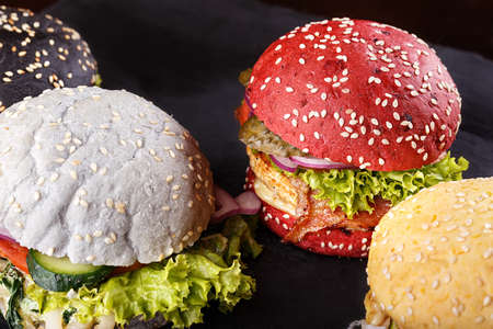 A lot of hamburgers based on different color buns, with vegetables, cheese, chops and meat is on a wooden board. Assortment of fast foodの写真素材