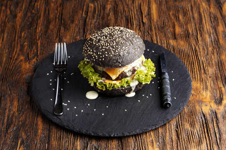 black burger with beef cutlet with vegetables, sesame, oil shale on the board on a dark backgroundの写真素材