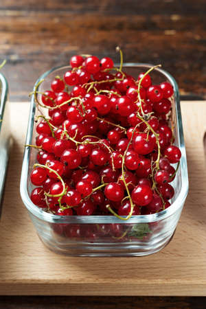 Ripe raw red currant in glass rectangular dishes on a wooden background, space for text