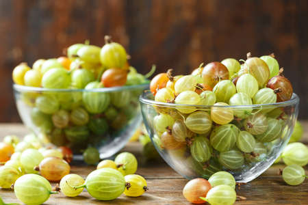 Ripe gooseberry in a glass plate and scattered next to a plate on a dark brown background, space for text. Gooseberry multicoloredの写真素材
