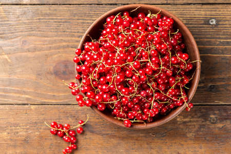 Red currant in a clay plate on a brown wooden kitchen table. top view