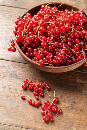 Red currant in a clay plate on a brown wooden kitchen table. Preparation of vitamin dessert.