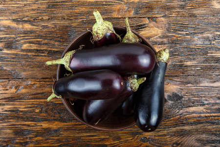 harvest of eggplant in a clay plate on an old dark wood tableの写真素材