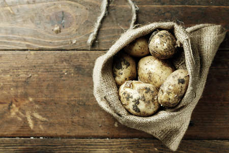 lot of young potatoes in a sackcloth sack on a wooden backgroundの写真素材