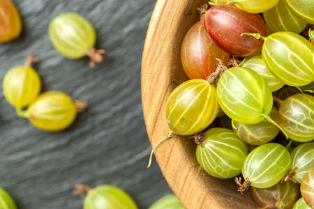 Ripe gooseberry in a wooden plate and scattered next to a plate on a black slate background, space for text. Gooseberry multicoloredの写真素材