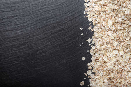 raw oatmeal is scattered on a black background, on slate blackboard, with space for textの写真素材