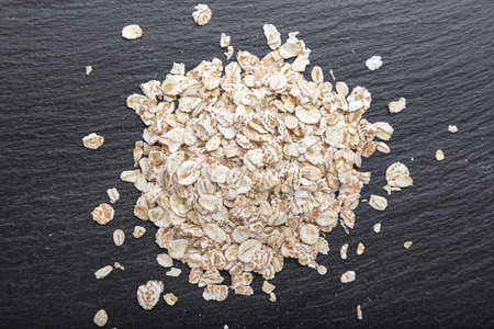 raw oatmeal is scattered on a black background, on slate blackboard, with space for text